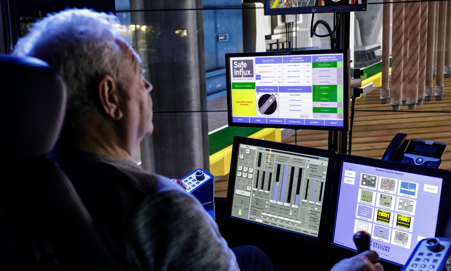 A man operates a control board with multiple screens and buttons. The screens display various charts, controls, and information, including one labeled "Safe Influx.
