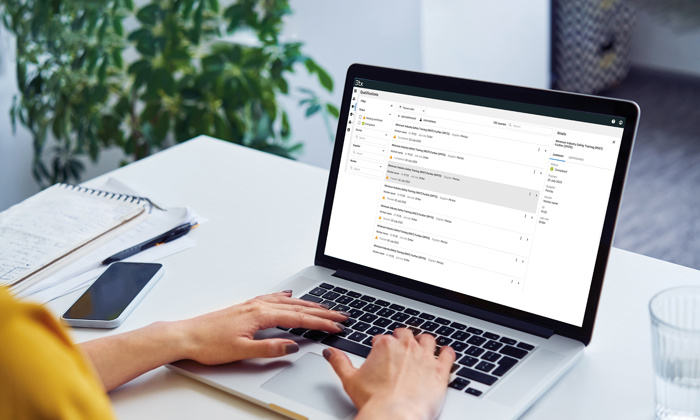 Personne tapant sur un ordinateur portable à un bureau avec une boîte de réception ouverte sur l'écran, à côté d'un carnet de notes, d'un stylo, d'un smartphone et d'un verre d'eau. Une plante se trouve à l'arrière-plan.