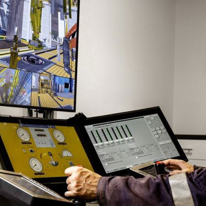 An operator closely monitors and controls machinery using multiple screens and controls in a high-tech industrial setting.