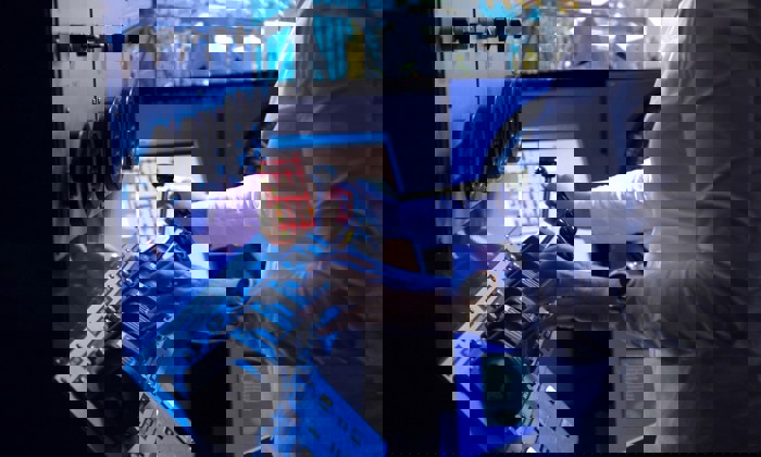 Person operating a control panel with switches and dials, wearing a white long-sleeve shirt and a smartwatch.