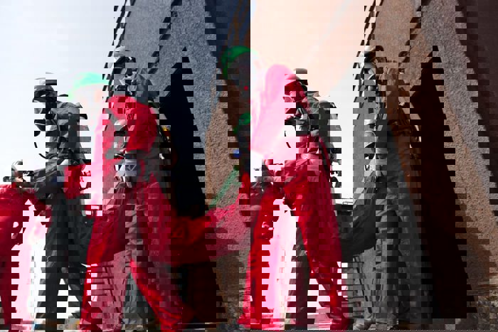 Emergency responders in red protective suits and green helmets carry an individual up a metal staircase.