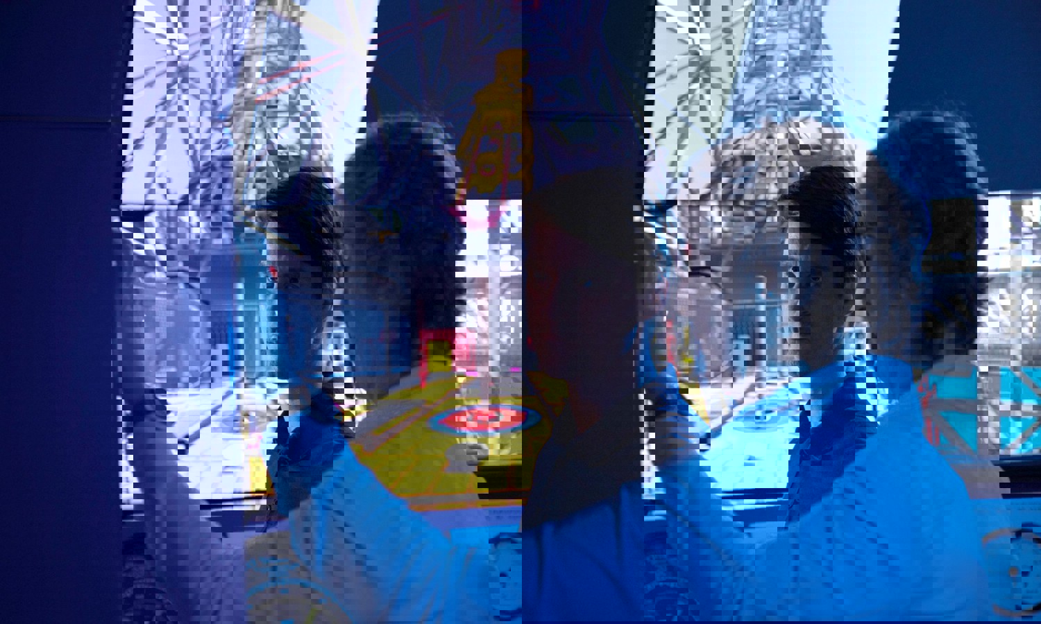 Dois homens numa sala de controlo operam um simulador com um grande ecrã que mostra o interior de um ambiente industrial. Um deles está a apontar enquanto o outro observa atentamente.