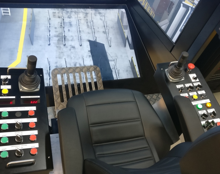 Interior view of a control cabin with two joysticks, multiple buttons, a seat, and a screen displaying equipment data.
